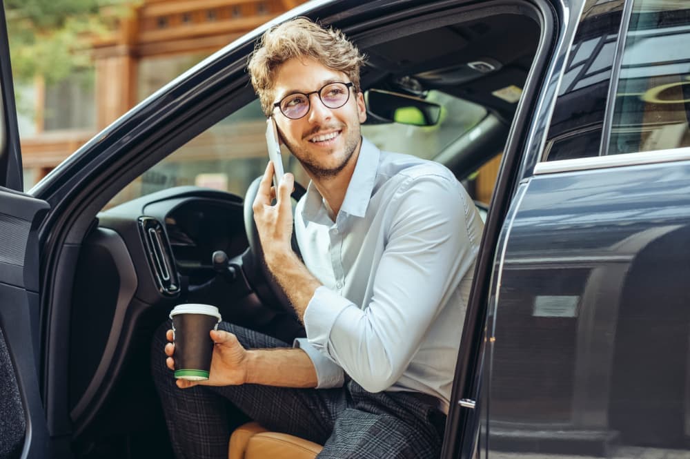 A man getting out of a car while holding a phone and coffee