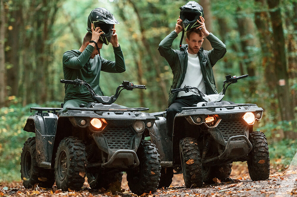 2 people riding ATVs in the woods.