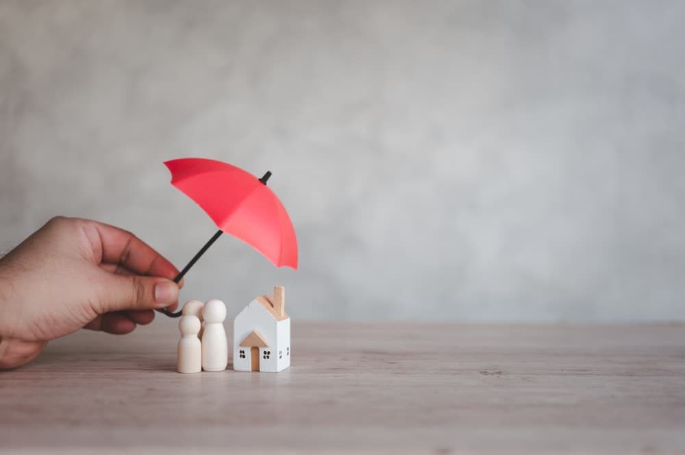 Tiny umbrella covering toy home symbolizing umbrella insurance coverage