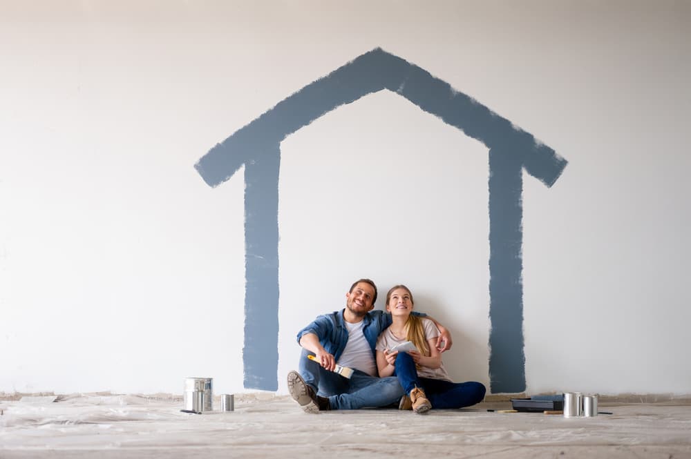 Couple sitting under blue house outline painted on white wall
