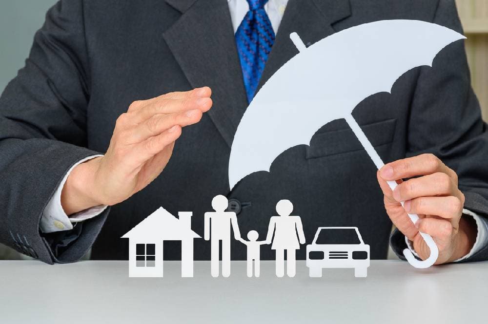 Insurance agent holding paper umbrella over paper cutouts of family