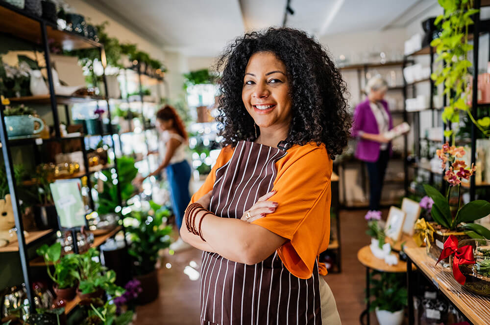 Woman standing in plant store with crossed arms.