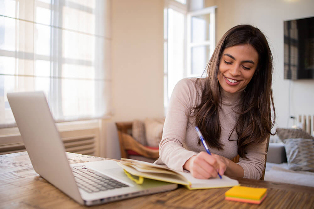 Young woman working from home in front of laptop on table.